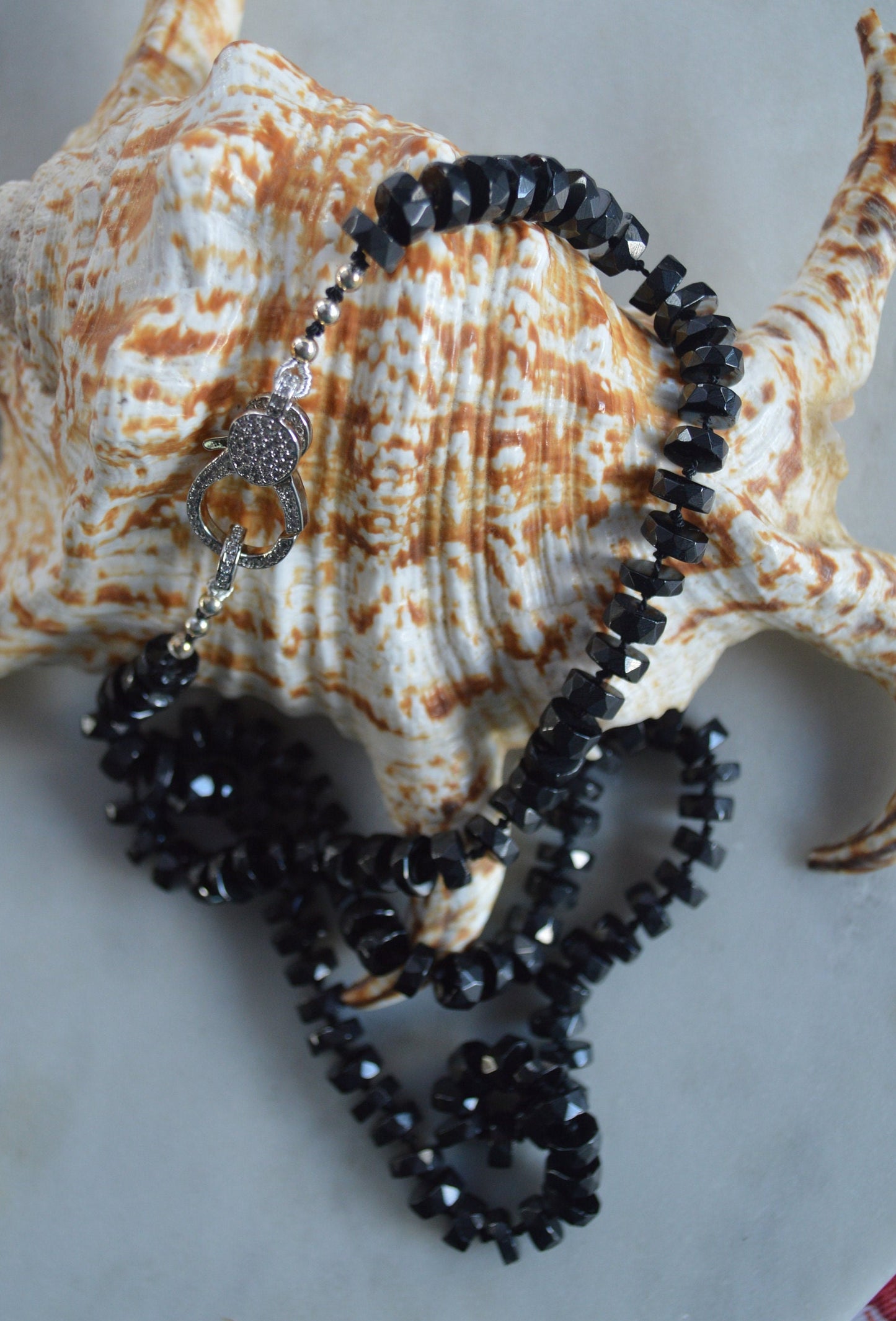 Black Spinel 7mm Faceted Heishi Beads Hand Knotted on Black Silk. Sparkly CZ Lobster Clasp Can Be Worn In Front With Charms, or In Back. 22"