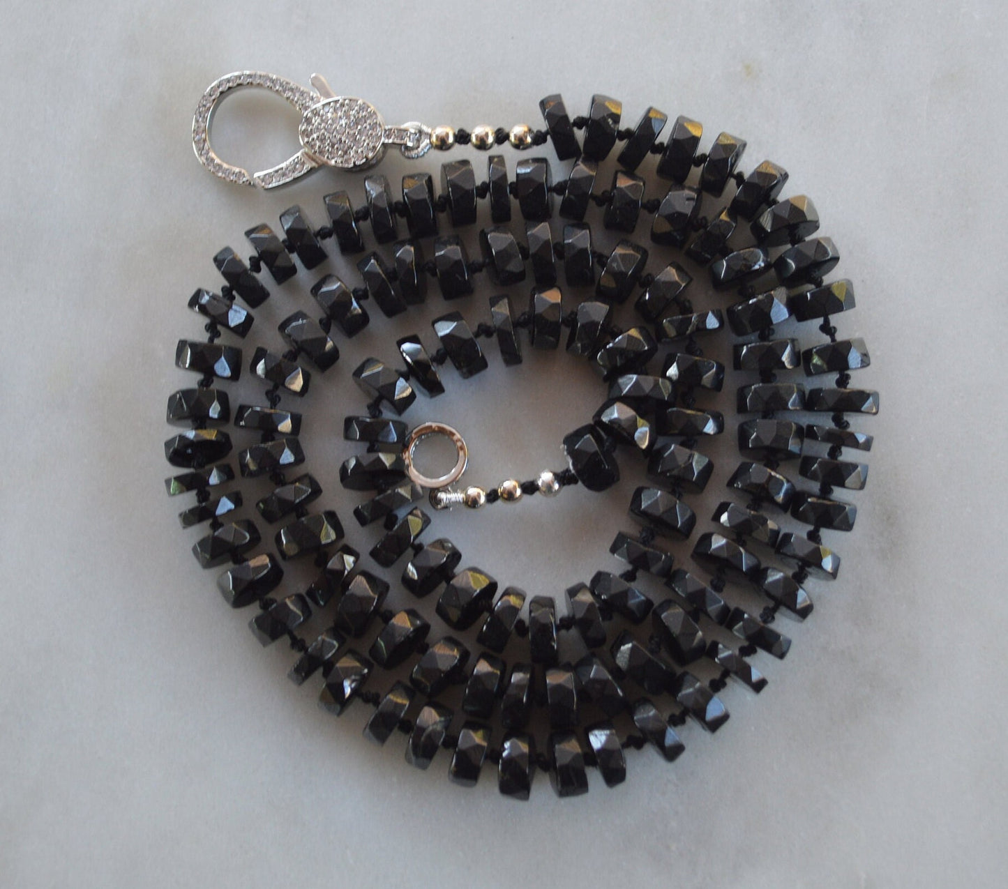 Black Spinel 7mm Faceted Heishi Beads Hand Knotted on Black Silk. Sparkly CZ Lobster Clasp Can Be Worn In Front With Charms, or In Back. 22"
