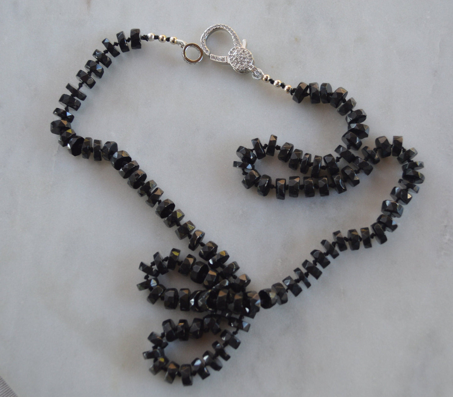 Black Spinel 7mm Faceted Heishi Beads Hand Knotted on Black Silk. Sparkly CZ Lobster Clasp Can Be Worn In Front With Charms, or In Back. 22"