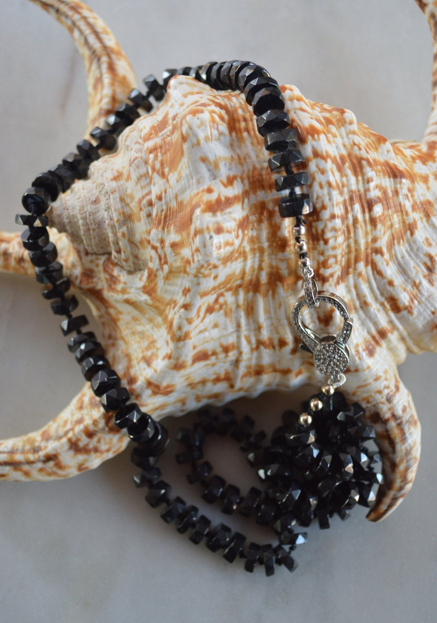 Black Spinel 7mm Faceted Heishi Beads Hand Knotted on Black Silk. Sparkly CZ Lobster Clasp Can Be Worn In Front With Charms, or In Back. 22"